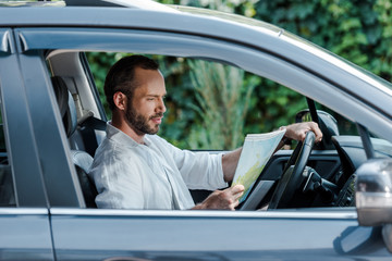 selective focus of bearded man driving car and looking at map