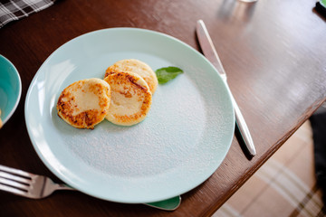 Three cottage cheese pancakes with shugar powder on a blue plate, top view. Syrniki. Copyspace horizontal top view curd pancakes