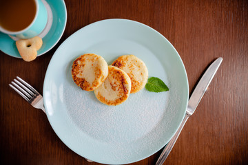 Three cottage cheese pancakes with shugar powder on a blue plate, top view. Syrniki. Copyspace horizontal top view curd pancakes