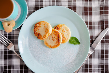 Three cottage cheese pancakes with shugar powder on a blue plate, top view. Syrniki. Copyspace horizontal top view curd pancakes