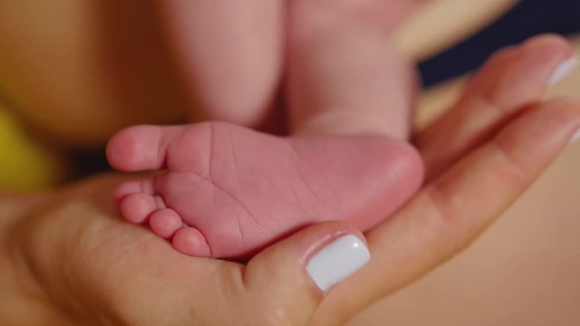 Baby feet in mother hands. Tiny Newborn Baby's feet on female Heart Shaped hands closeup. Mom and her Child. Happy Family concept. Beautiful conceptual video of Maternity. Close up shot.