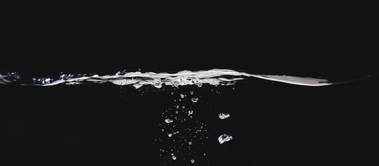 Waving liquid surface isolated on black background, close up view. Small water bubbles underwater....