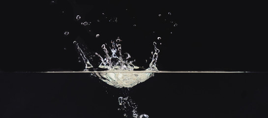 Water splash on liquid surface isolated on black background, close up view. Water bubbles in air,...
