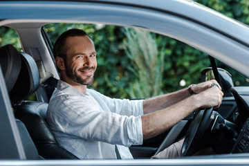 selective focus of happy bearded man smiling and looking at camera while driving car