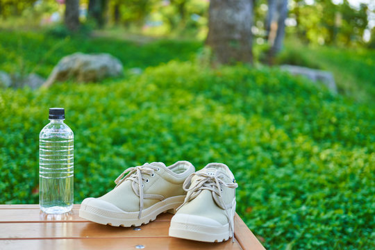 公園のテーブルの上に置かれたプラスチックボトルとシューズ。水分補給や健康、運動などを想起させる画像。