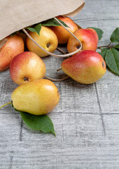 Still life of yellow-red pears with green leaves. Ripe juicy pears are scattered from a paper bag on a wooden table. Flat lay. Copy space.