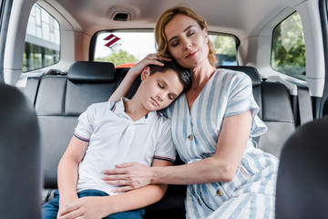 selective focus of mother and son with closed eyes in car