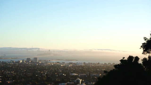 Sun setting over San Francisco and the Golden Gate Bridge on a clear Summer night, fog rolling into the Bay from the Pacific Ocean. Seen from Berkeley Hills, California.