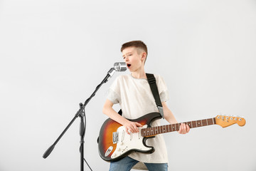 Teenage boy playing guitar and singing against light background