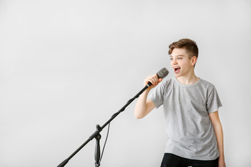 Teenage boy with microphone singing against light background