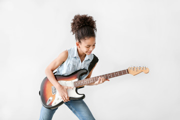 African-American girl playing guitar against light background