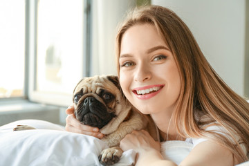 Morning of beautiful young woman with cute pug dog in bedroom