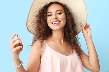 Happy African-American woman with perfume bottle on color background