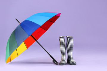 Stylish umbrella with gumboots on color background