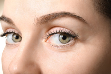 Beautiful young woman with eyelash extensions on white background, closeup