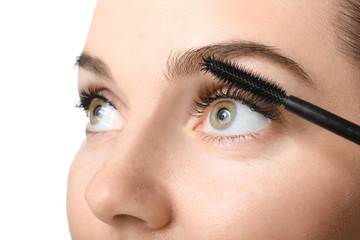 Beautiful young woman with eyelash extensions applying mascara against white background, closeup