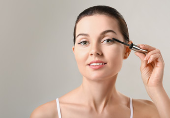 Fototapeta premium Beautiful young woman with eyelash extensions applying mascara against grey background