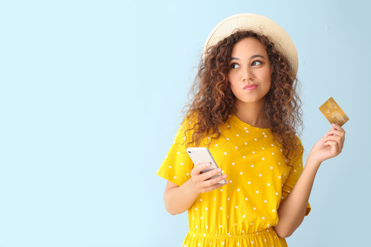 Thoughtful African-American woman with credit card and mobile phone on light color background