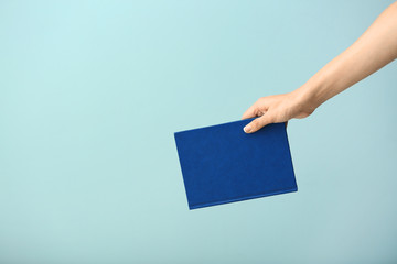 Female hand with book on color background