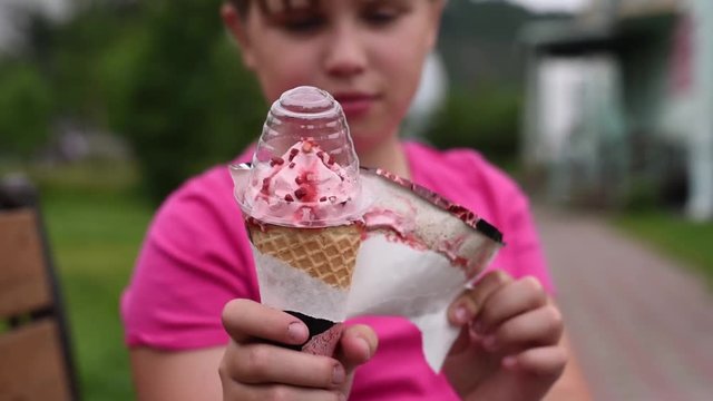 The girlie wants to eat ice cream. The girl removes the wrapper from strawberry ice cream.