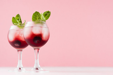 Fresh summer blueberry homemade lemonades in two goblets with ice cubes, berry, green mint in elegant pastel pink color kitchen interior.