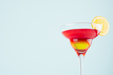 Alcohol cocktail for celebration  with red and yellow liquor, orange slice in mint color background, closeup, edge, details.