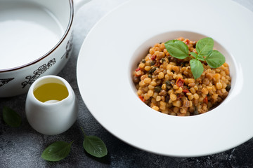 Fregola pasta with bell pepper, capers, green basil and olive oil, studio shot