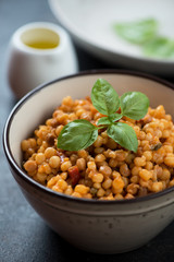 Bowl of italian fregola pasta with fresh green basil and olive oil, closeup, vertical shot