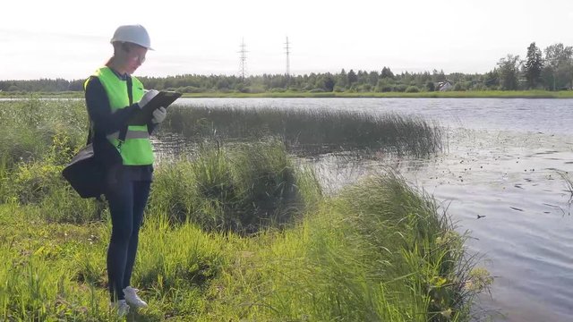 The ecologist carries out a visual express analysis of water in a reservoir and river. The data of the inspection of the coastal territory and the results of the analysis are recorded.