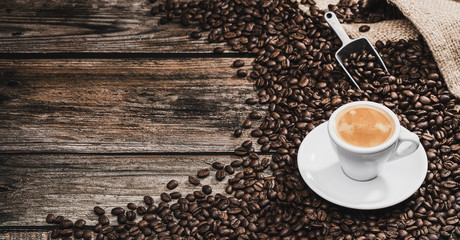 Espresso shot in coffee cup and coffee beans with coffee spoon on brown wooden background