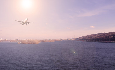 Fototapeta na wymiar Airliner over the river in the city. Sunset.
