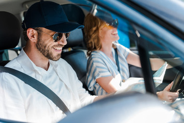 selective focus of happy man in sunglasses smiling with woman in car
