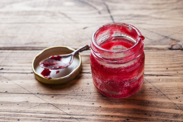 Empty jar of blueberry jam and a spoon on a wooden table.