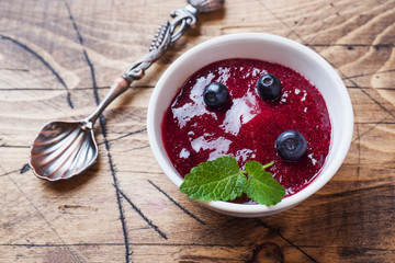 Blueberry jam in a plate and fresh blueberries on a wooden table.