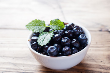 Fresh blueberries in a plate and mint leaves on a wooden background.