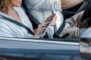 cropped view of woman using digital tablet near driver in car