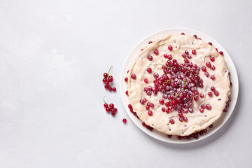 Delicious homemade tart with red currants and meringue, decorated with fresh berries, sprinkled with powdered sugar on a white plate on a light gray background, top view	