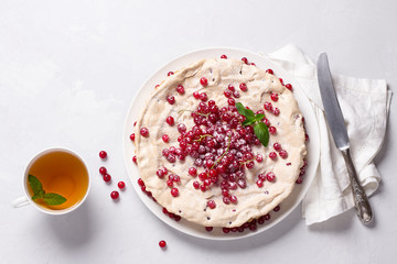 Delicious homemade tart with red currants and meringue, decorated with fresh berries, sprinkled with powdered sugar on a white plate on a light gray background, top view	