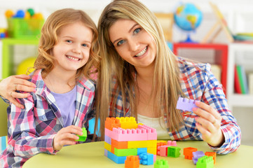 Cute little girl and her mother playing colorful plastic blocks
