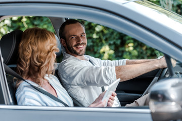 selective focus of happy man driving car and looking at woman with digital tablet