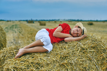Naklejka na ściany i meble Portrait of a little boy on vacation in the field . The child sleeps in the hay . Healthy sleep in the fresh air .