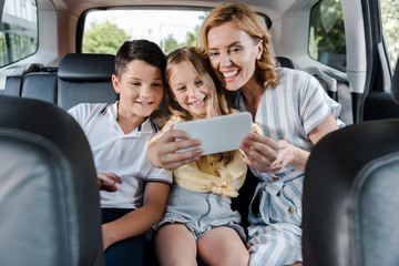 selective focus of cheerful family taking selfie on smartphone in car