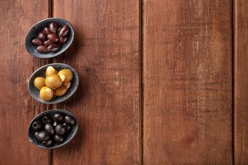 Various types of olives in bowls, shot from the top on a dark rustic wooden background with copy space. Purple, green almond stuffed, and black pitted olives with a place for text