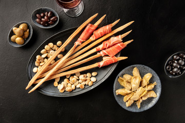 Italian antipasti. Prosciutto-wrapped Italian grissini with olives, artichokes, and wine, shot from the top on a black background