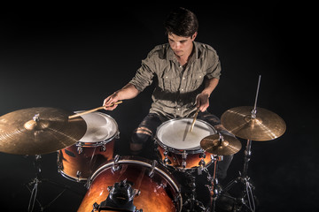 Professional drummer playing on drum set on stage on the black background