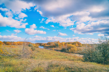 Autumn landscape. Blue sky with clouds, small river, orange leaves on trees