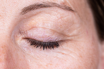 Fototapeta na wymiar A close-up view on the closed eye of a mature woman in her mid forties. Details of the aging process of the skin. Wrinkles, liver spots and imperfections.