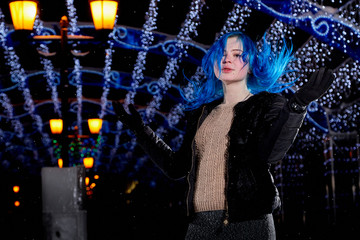 Girl with blut hair skating on the ice arena in the evening city square in winter