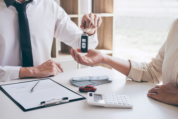 Agent holding key of new car giving to woman client after signing contract