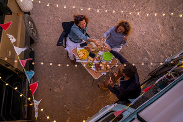 Group of friends having dinner together in friendship outside little van - alternative travel...